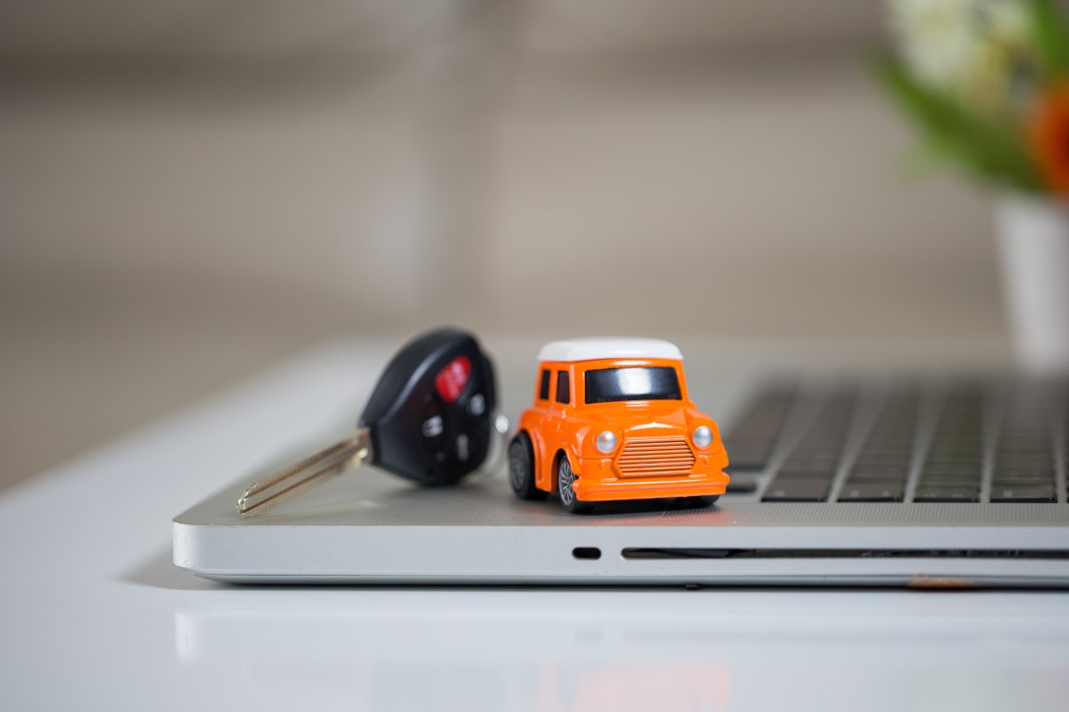 Miniature car and car keys on laptop keyboard